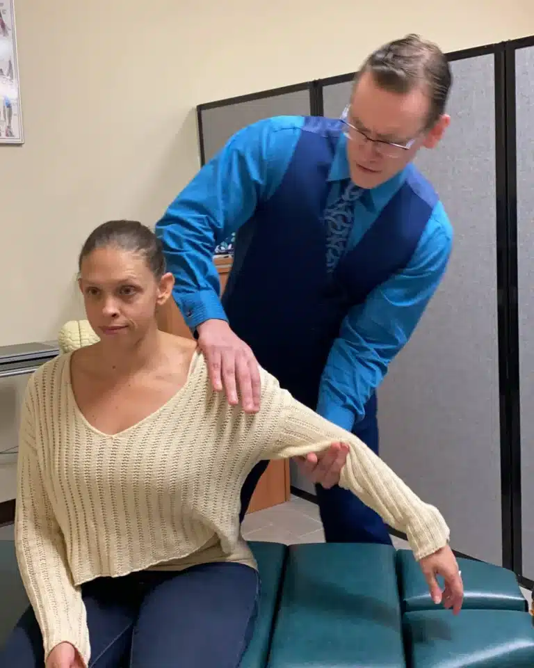 Dr. Michael Brandon, D.C., assessing a seated patient's shoulder